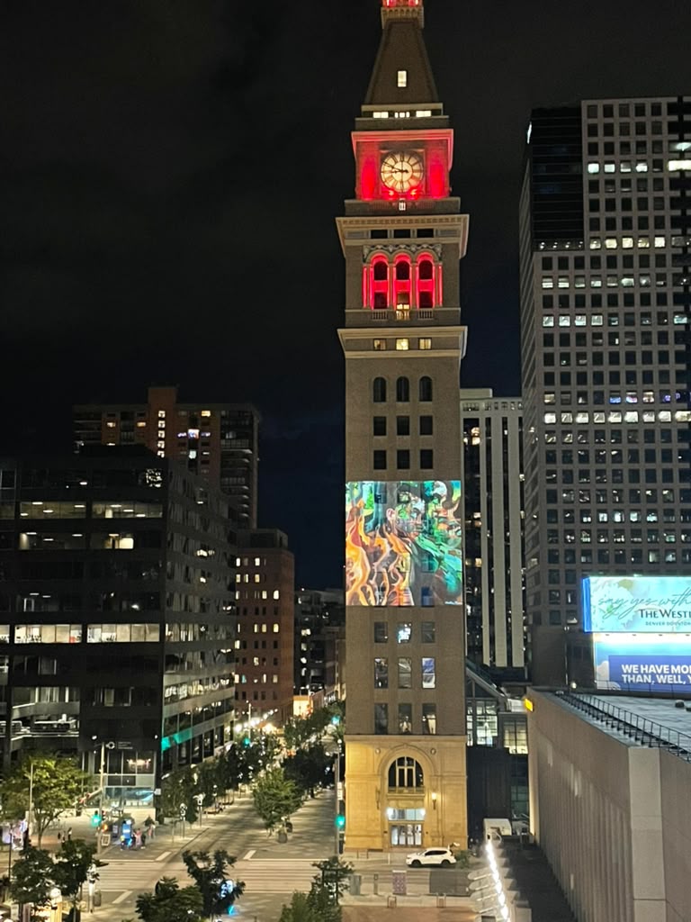 A torre do relógio Daniels and Fisher, em Denver, à noite, com uma pintura colorida de Caroline Moran projetada na fachada