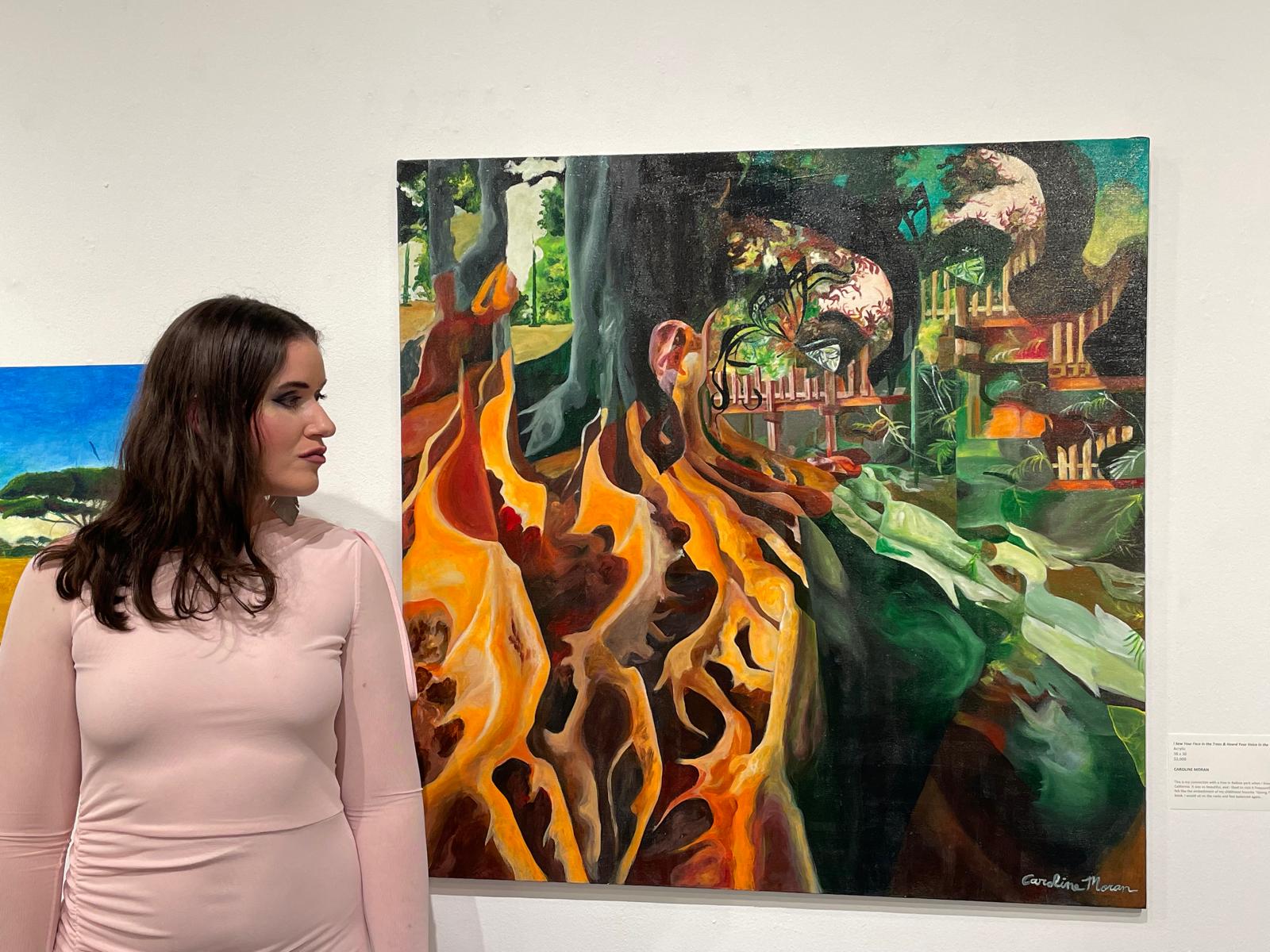 Caroline Moran, de perfil, ao lado de uma grande tela em tons de laranja e verde numa exposição